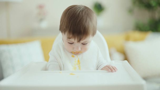 Adorable hispanic toddler sitting on highchair eating food at home - Foto, afbeelding
