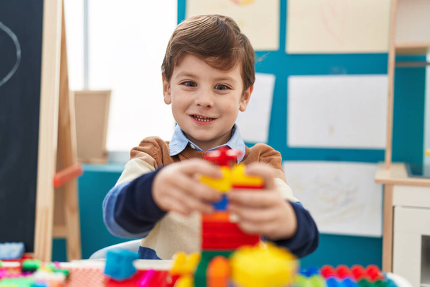 Adorable niño hispano jugando con bloques de construcción sentado en la mesa en el jardín de infantes - Foto, Imagen