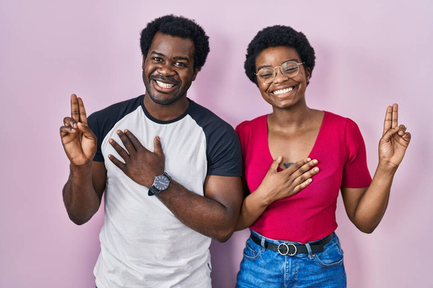 Young african american couple standing over pink background smiling swearing with hand on chest and fingers up, making a loyalty promise oath  - Foto, Bild