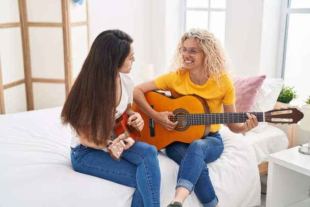 Dwie kobiety matka i córka grają na gitarze klasycznej i ukulele w sypialni - Zdjęcie, obraz