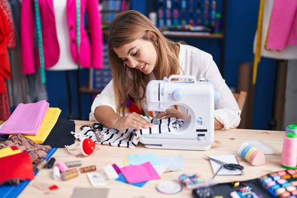Jeune femme tailleur souriant confiant en utilisant une machine à coudre au studio de couture - Photo, image