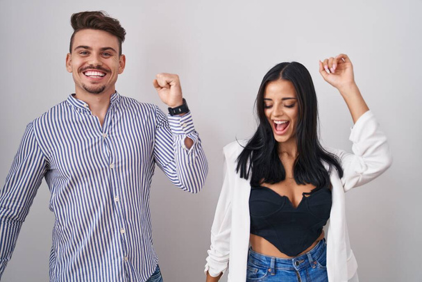 Fiatal spanyol pár áll fehér háttér tánc boldog és vidám, mosolygós mozgó alkalmi és magabiztos zenét hallgatni  - Fotó, kép