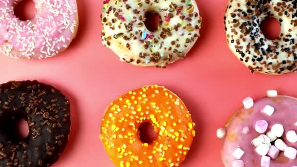 Verschiedene frische, leckere süße Donuts in einer Reihe. Stop-Motion. Donuts aus verschieden beweglichen, vier glasierten süßen Donuts. Bäckerei- und Lebensmittelkonzept. Ansicht von oben. Schokolade, rosa, blaue Donuts in der Packung. 4K, UHD Draufsicht rosa Hintergrund drehen - Filmmaterial, Video