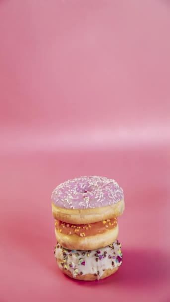 Ciambelle dolci impilate l'una sopra l'altra sotto forma di torre, ciambelle video verticali gustosi deliziosi snack dolci caramelle su sfondo rosa - Filmati, video