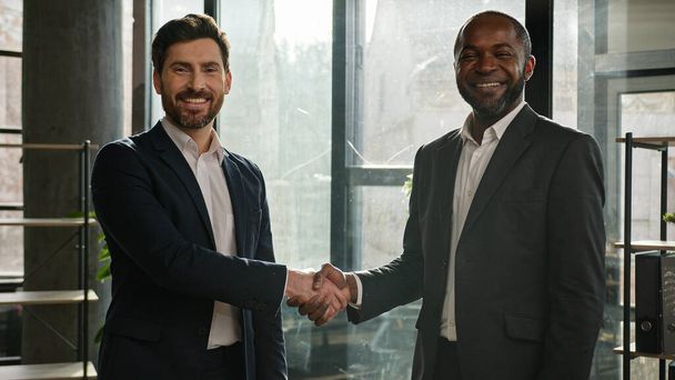 Két boldog mosolygós, sokszínű üzletember többnemzetiségű partnerek férfiak kaukázusi és afro-amerikai üzletemberek az irodában kezet ráznak mosolygós kézfogás megállapodás kézfogás partnerség - Fotó, kép
