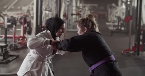 Zoom in view of Muslim female fighter throwing away hands of opponent while sparring during BJJ training in gym - Video