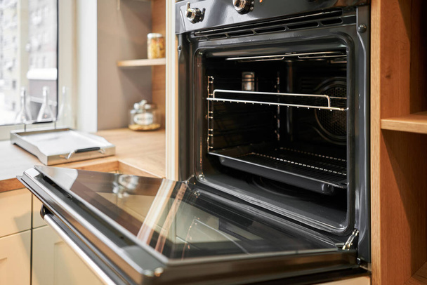  Opened door at electric oven with air ventilation. Side view of modern technology appliance against kitchen furniture. High quality photo - Zdjęcie, obraz
