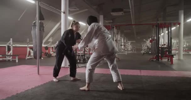 Handheld-Aufnahme von barfuß verschiedenen Kämpferinnen beim heimlichen Händeschütteln während des brasilianischen Jiu-Jitsu-Trainings in der geräumigen Turnhalle - Filmmaterial, Video
