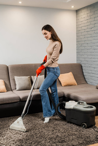 Housewife dry cleaning of carpet and removing dust, stains and dirt using mop extractor machine. Cleaner girl is cleaning carpet with mop extractor dry cleaning machine at clients home - Fotó, kép