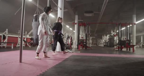 Tracking shot of diverse women doing front rolls on floor during BJJ training in gym - Video