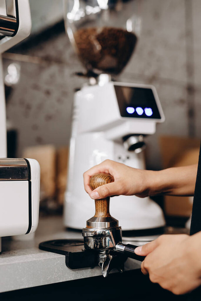 Κοντινό πλάνο του χεριού Barista καφέ κάνοντας καφέ με το χέρι πατητήρια αλεσμένο καφέ χρησιμοποιώντας πλαστογράφηση στο καφενείο. - Φωτογραφία, εικόνα