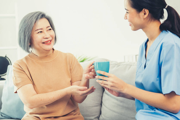 Жіночий догляд за жінкою, що подає їй задоволеного старшого пацієнта з чашкою кави вдома, посміхається один одному. Медична допомога для пенсіонерів, служба охорони здоров'я
. - Фото, зображення