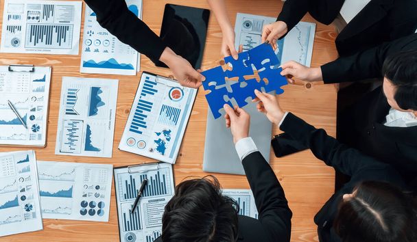 Top view businesspeople and colleagues in formal wear putting jigsaw puzzles together over meeting table with financial report papers in harmony office for team building concept. - Fotografie, Obrázek