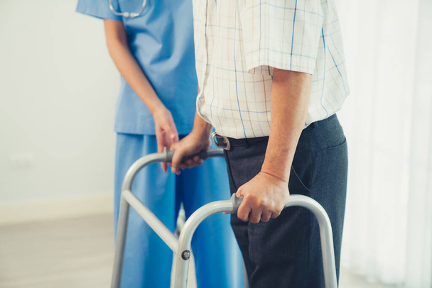 Physiotherapist assists her contented senior patient on folding walker. Recuperation for elderly, seniors care, nursing home. - Foto, Imagen