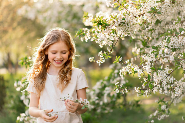 Glückliches schönes Mädchen lächelt und pflückt Blumen im Frühling blühende Kirschbäume Garten, Kopierraum - Foto, Bild