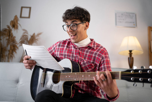 Man with guitar holding music book with notes at home have an idea. Copy space - Foto, imagen