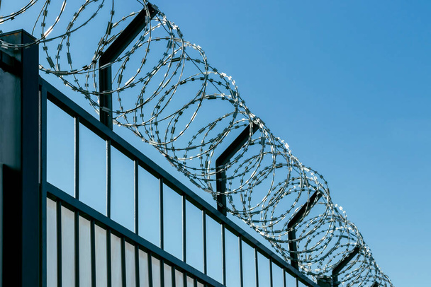 Barbed wire on an iron fence. Against the background of the blue sky. - 写真・画像