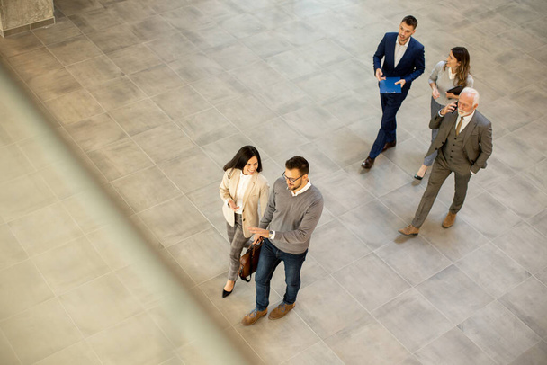 Group of young and senior business people are walking in an office hallway, captured in an aerial view. They are dressed in formal attire, walking with purpose and intent and discussing amongst themselves and interacting with colleagues - Fotografie, Obrázek