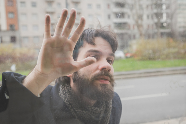 Молодой красивый бородатый мужчина позирует за стеклом
 - Фото, изображение