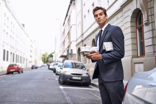 On a coffee run. A handsome businessman in s suit standing with his coffee and newspaper in a city street - Photo, Image