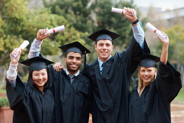 Делятся своими достижениями. Группа выпускников колледжа, стоящих в шапке и халате и держащих дипломы - Фото, изображение