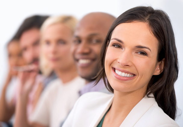 She feels fresh and confident in the corporate world. Portrait of an attractive business woman smiling at the camera with a row of business people behind her - Photo, Image