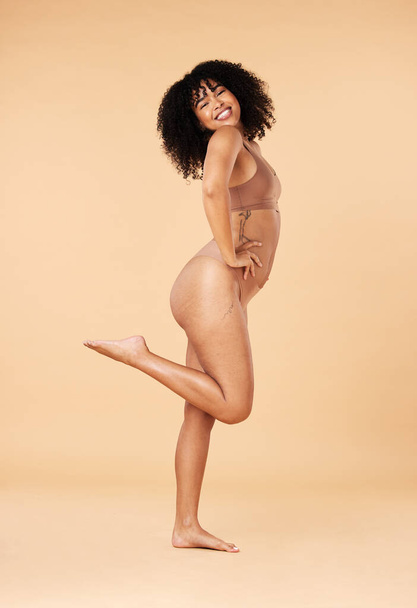 Positiviteit van het lichaam, zelfverzekerd en portret van een vrouw in ondergoed geïsoleerd op een beige studio achtergrond. Vrolijk, glimlach en lingerie model met vrijheid, geluk en aantrekkelijk in bikini mode. - Foto, afbeelding