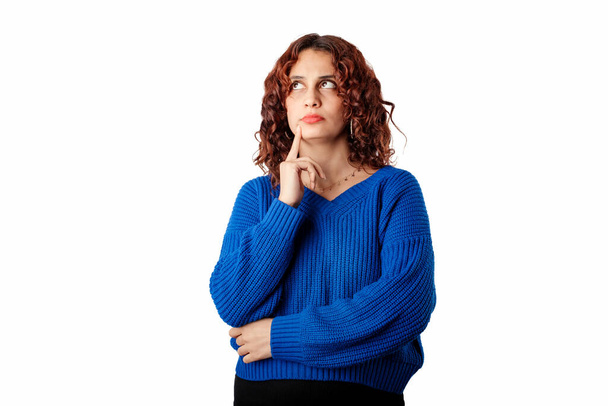Молода красива жінка в блакитному светрі ізольована на білому тлі нерозв'язана, гаманці губ і дотики з індексним пальцем. Дивиться на порожній простір копіювання і намагається вирішити
. - Фото, зображення