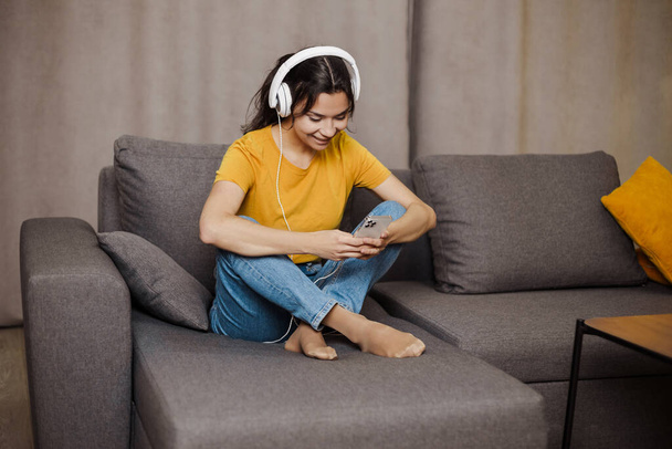 Счастливая индийская или арабская девушка отдыхает на уютном диване дома, слушая музыку - Фото, изображение