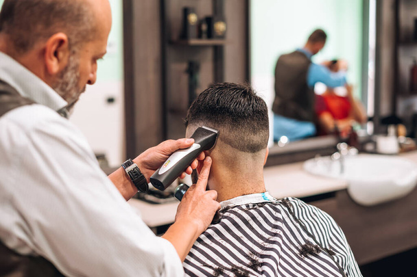 仕事中現代理容室における男性クライアントの暗い髪をトリミング作物理髪店のバックビュー - 写真・画像