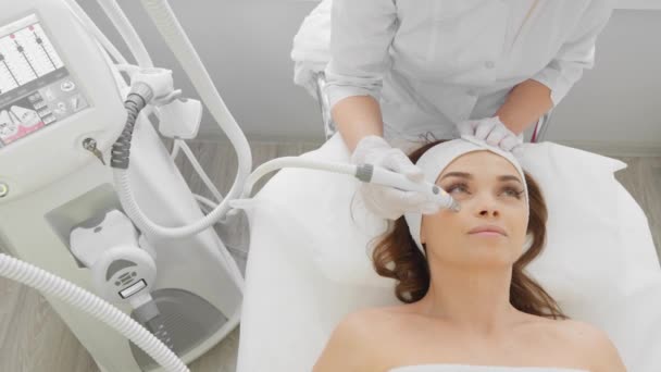 Radiofrequency facial skin lifting. Hardware cosmetology RF lifting procedure and hardware facial massage. Rejuvenation, skin care in a beauty salon. Woman doctor cosmetologist and girl in spa clinic. - Materiaali, video