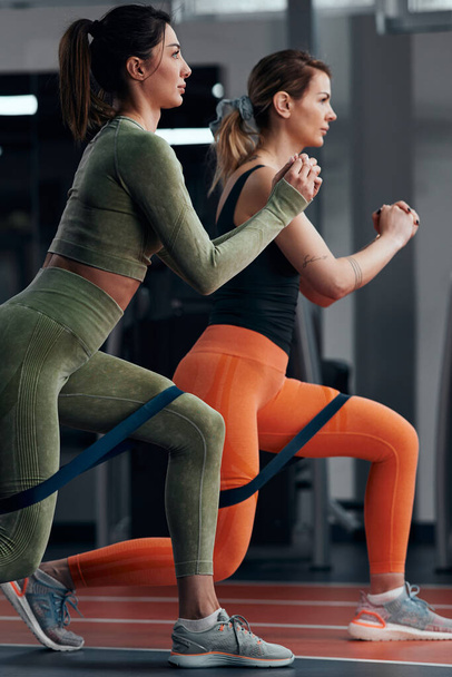 Spor salonundaki sporcu kadınlar elastik direnç lastiğiyle egzersiz yapıyorlar.. - Fotoğraf, Görsel