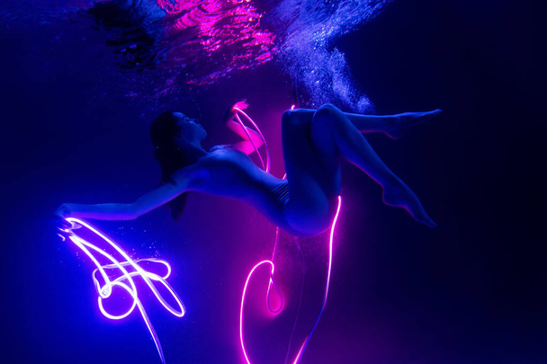 Gymnast shows underwater performance in neon light. Soft blurred focus - Photo, image