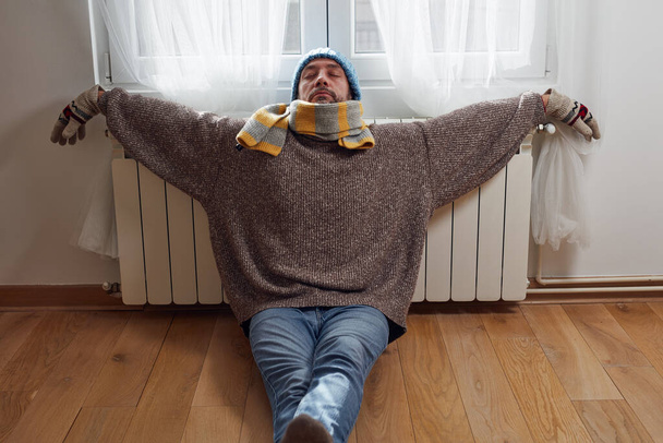 Serin bir kış gününde şapkalı, kazaklı ve eldivenli bir adam, enerji ve gaz krizi, soğuk oda, ısıtma sorunları. - Fotoğraf, Görsel
