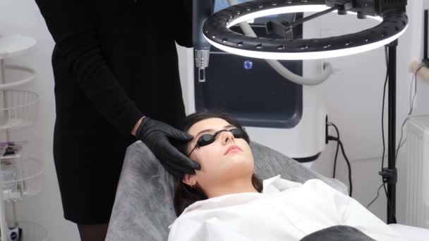 Een jong meisje in een schoonheidssalon met een beschermende bril. Lasergezichtshaar verwijderen procedure met behulp van moderne technologieën - Video
