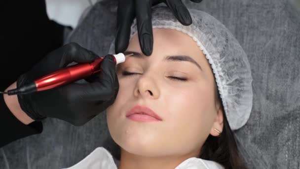 Eyebrow coloring procedure in a beauty salon. The hand of a master paints the eyebrows of a young beautiful girl with the help of modern devices. Modern technologies in cosmetology - Filmati, video