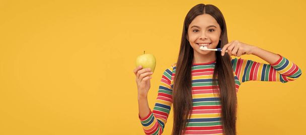 Happy girl child brush teeth with toothbrush holding apple yellow background, healthy teeth. Banner of child girl with teeth brush, studio portrait, header with copy space - Photo, image