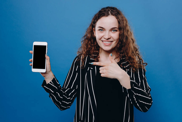 Крупним планом чарівна молода щаслива жінка тримає телефон вказуючи пальцем на екрані ізольовано на фоні
 - Фото, зображення