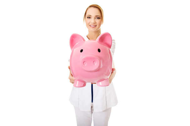 Young female doctor holding a piggybank. - Photo, Image