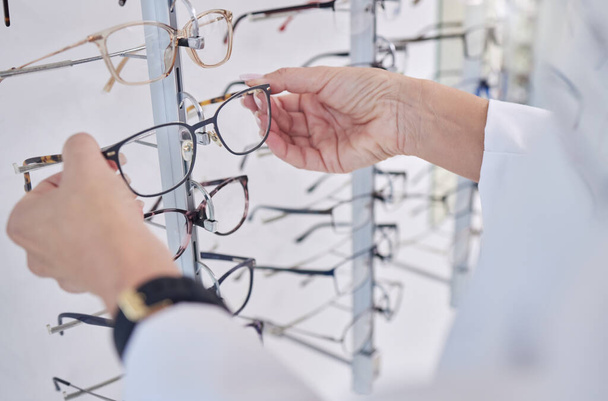 Working, decision and hands of an optometrist with glasses, eyewear and frame for vision in a shop. Healthcare, retail and optician with a choice of eyeglasses for visual service and optics in store. - Foto, Imagen