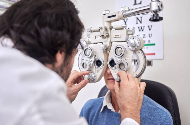 Οφθαλμική φροντίδα, εξέταση ή εξέταση για οφθαλμολογική εξέταση ασθενούς και γιατρού AT για οπτική εξέταση φακού ή πλαισίου. Γυναίκα και άνθρωπος υγειονομική περίθαλψη πρόσωπο με μηχάνημα για τα μάτια, την όραση και την υγειονομική ασφάλιση εξέταση. - Φωτογραφία, εικόνα