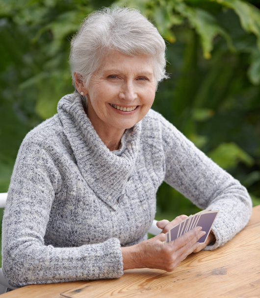 Umie grać w karty. Portret starszej kobiety trzymającej dłoń z kart siedzącej na patio - Zdjęcie, obraz