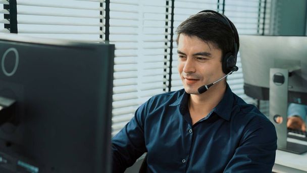 Young competent asian male call center agent working at his computer while simultaneously speaking with customers. Concept of an operator, customer service agent working in the office with headset. - Foto, imagen