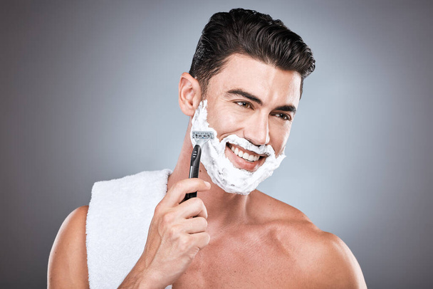 Shaving cream, face and man with razor in studio isolated on a gray background. Epilation, cleaning and thinking male model with facial product, foam or gel to shave for wellness and hair removal - Fotó, kép