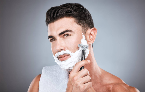 Face, shaving cream and man with razor in studio isolated on a gray background. Skincare, cleaning and thinking male model with facial product, foam or gel to shave for wellness, health and hygiene - Fotó, kép