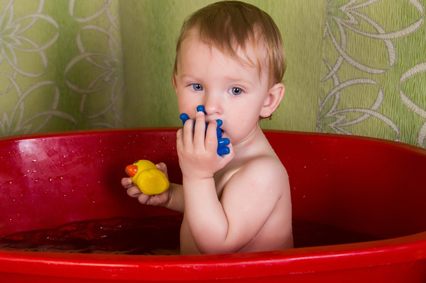 Την όμορφη μικρή ξανθιά κοπέλα κάθεται στο μπάνιο και μασάτε παιχνιδιών - Φωτογραφία, εικόνα