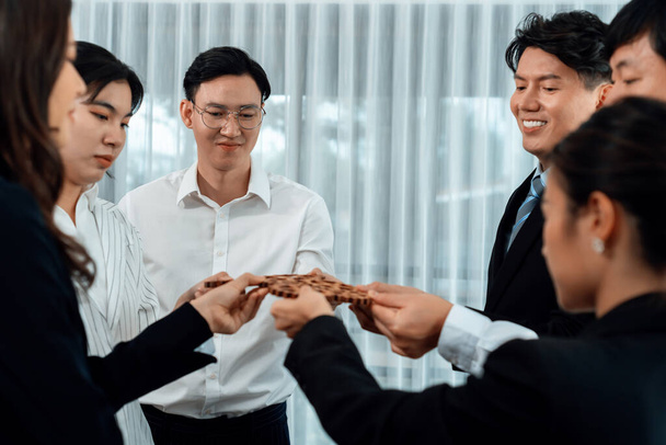 Closeup hand holding wooden gear by businesspeople wearing suit for harmony synergy in office workplace concept. Group of people hand making chain of gears into collective form for unity symbol. - Fotó, kép