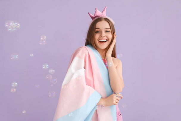 Молодая женщина в короне с трансгендерным флагом и мыльными пузырями на сиреневом фоне - Фото, изображение