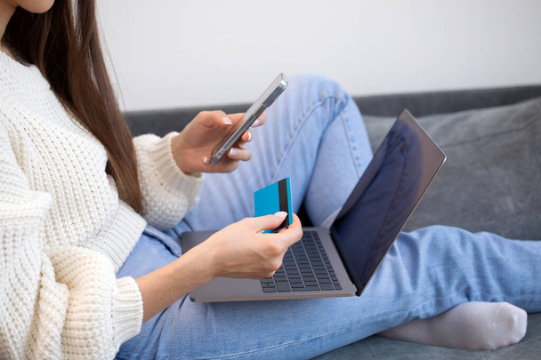 Online payment, a woman holds a smartphone and uses a credit card for online purchases. The concept of online shopping, online payment using a laptop computer - Photo, Image