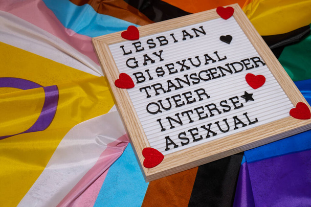 絹素材で作られたレインボーLGBTQIAフラグ上のLGBTQIAの説明フレーム。レズビアン、ゲイ、バイセクシャル、トランスジェンダー、クィア、インターセックス、セクシュアル。LGBTQプライド月間のシンボル。平等な権利。平和と自由。LGBTQIAコミュニティを支援する。多様性平等 - 写真・画像